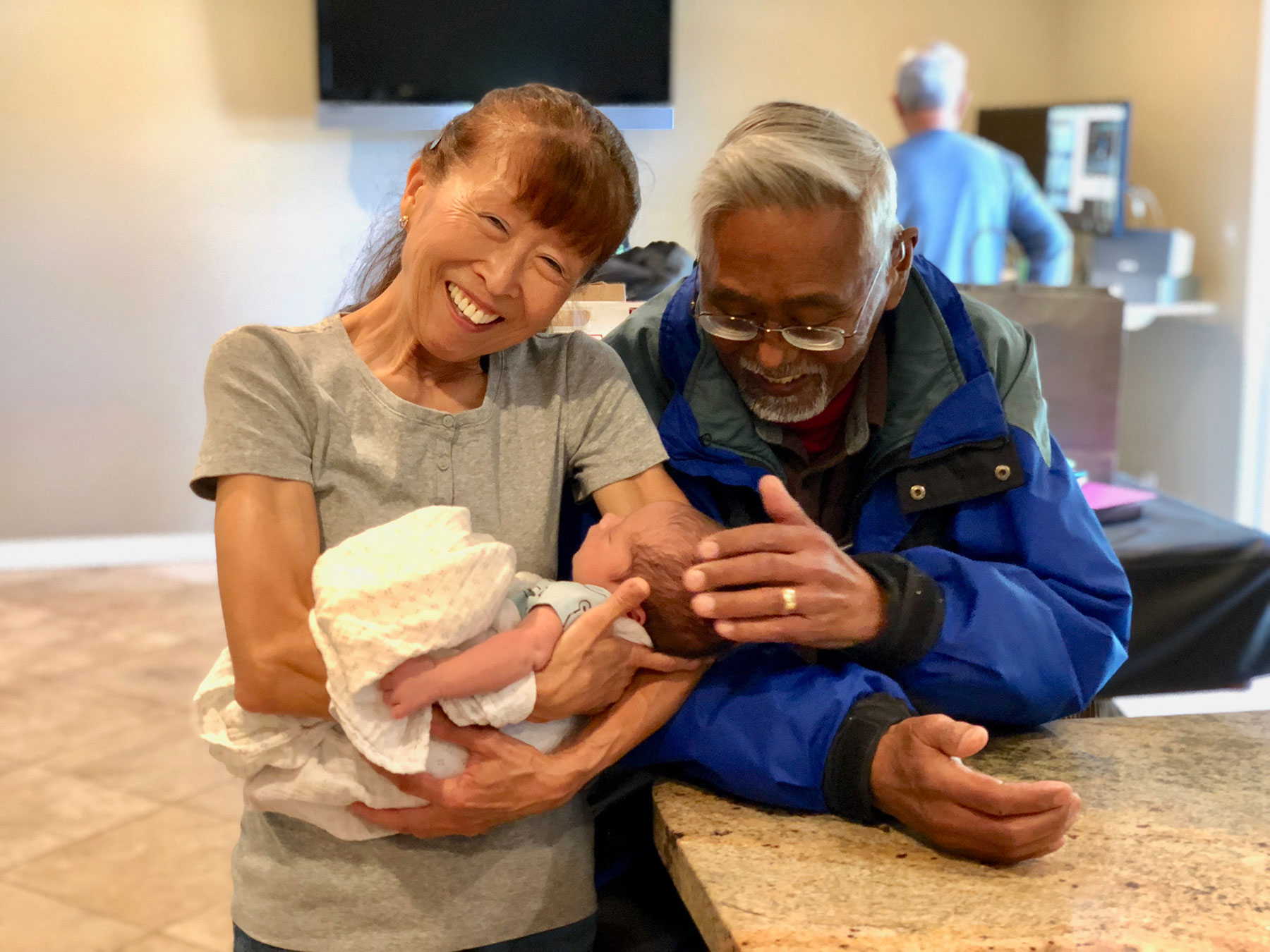 Two adults smiling as they hold a baby together.